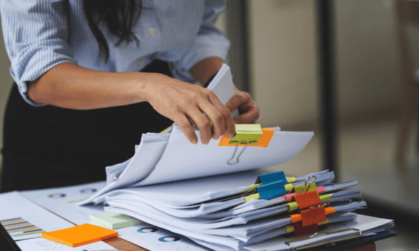 Teacher manually goes through a stack of Master Agreements stacked on her desk.